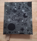 Front of small gray handmade journal with black moons and black and silver-toned stars