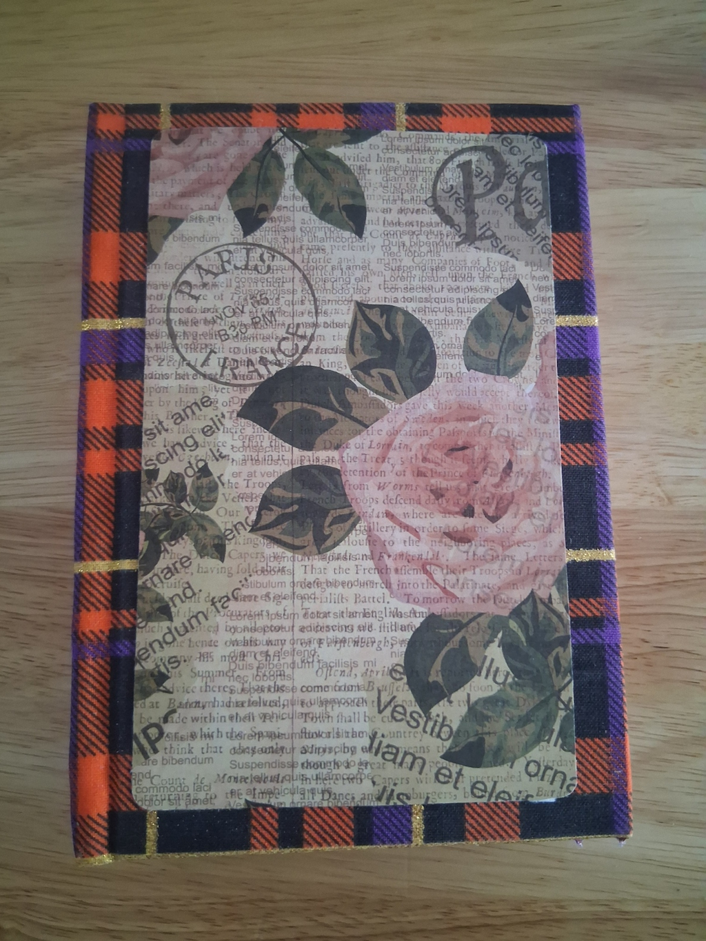 Front of handmade journal with rose and newsprint-style panel over orange, purple, and black plaid
