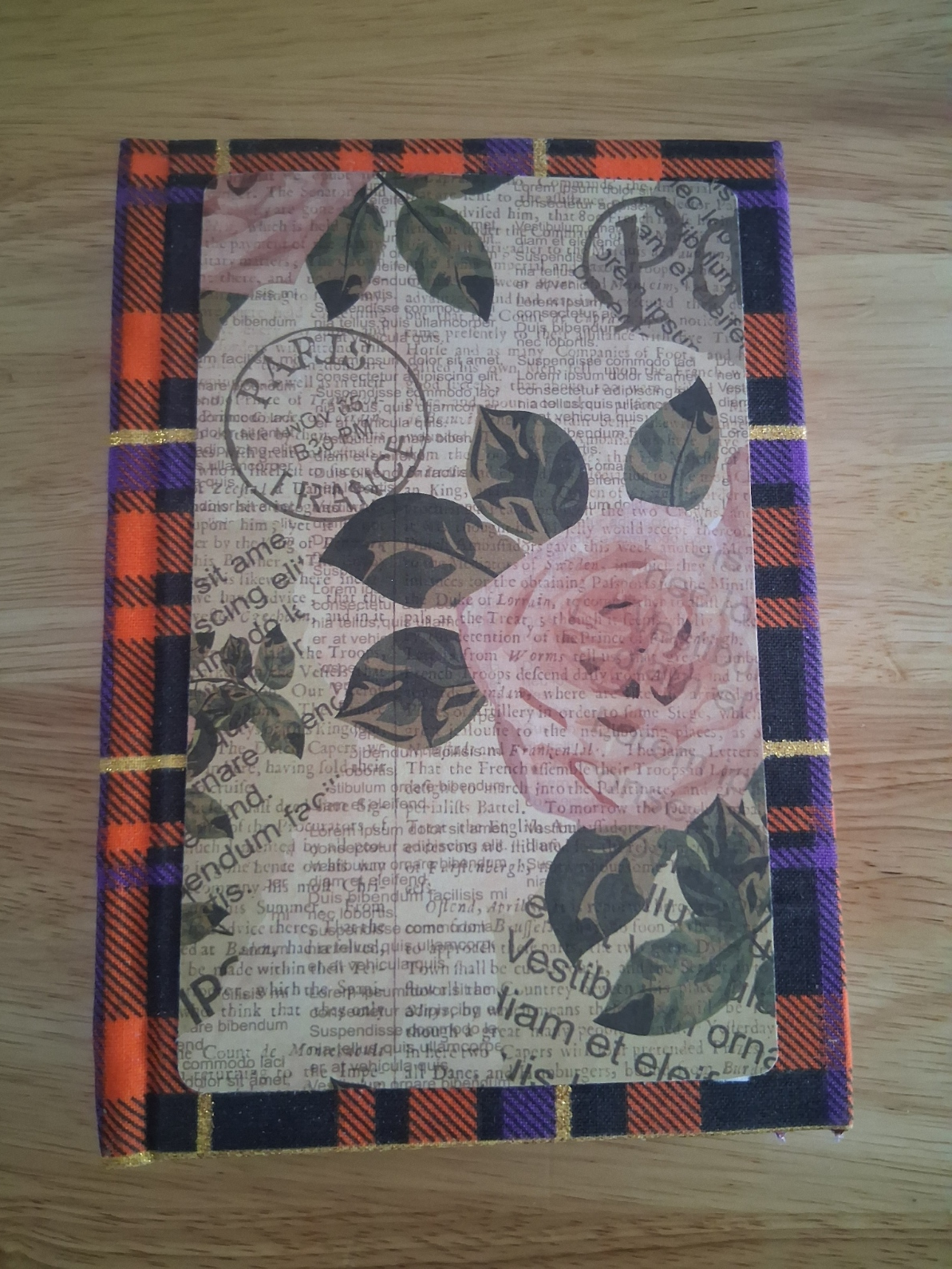 Front of handmade journal with rose and newsprint-style panel over orange, purple, and black plaid